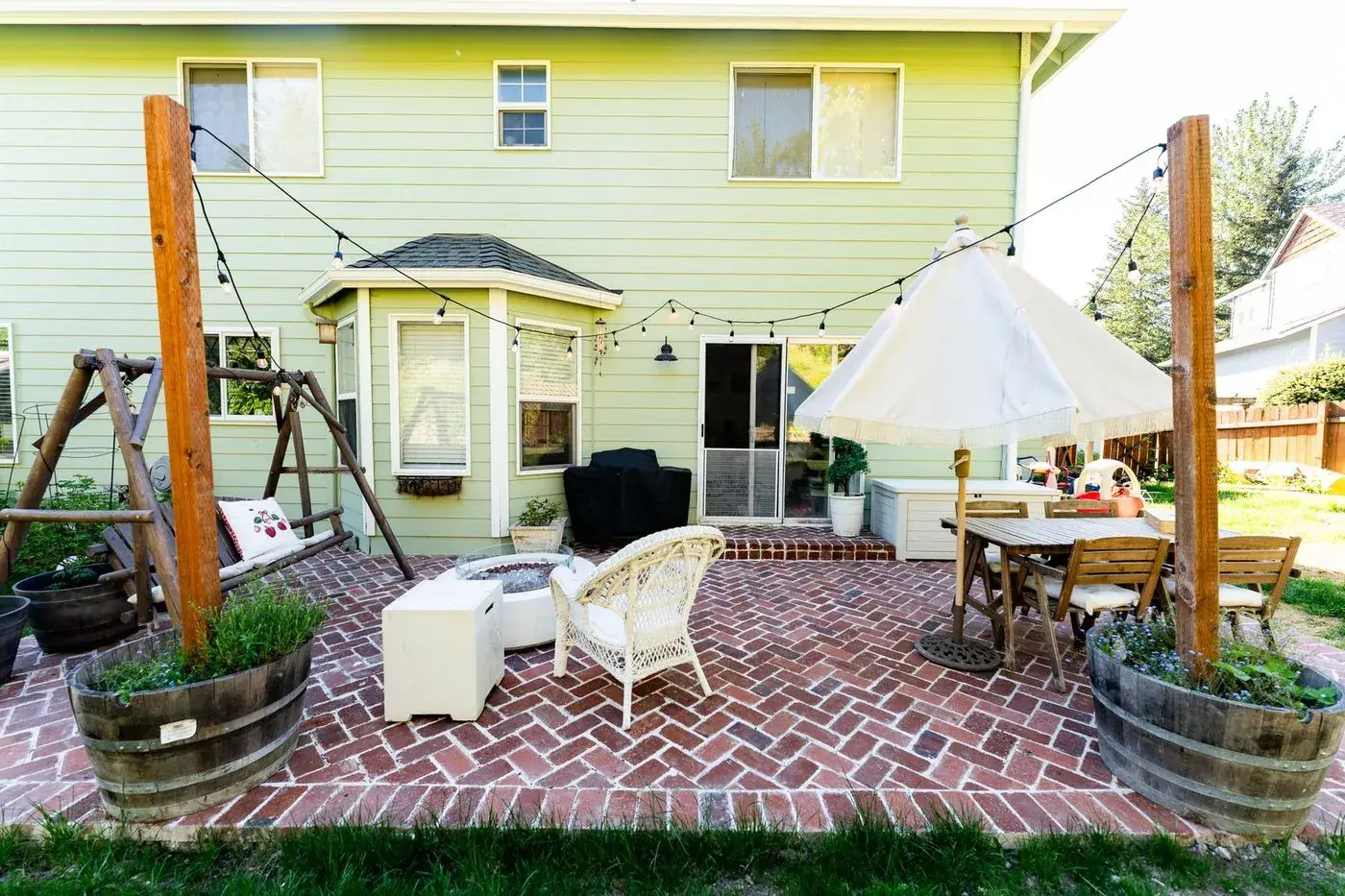 Herringbone brick patio with string lights, fire table and swing