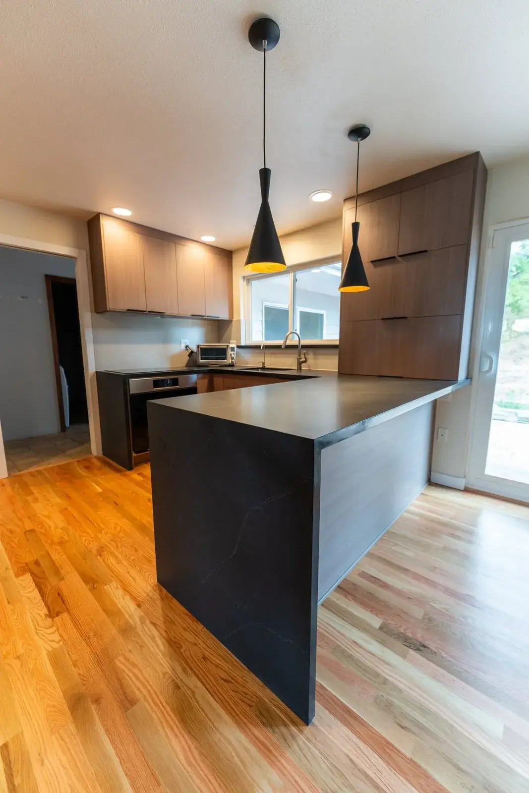 Black quartz waterfall peninsula with walnut cabinetry and black pendants