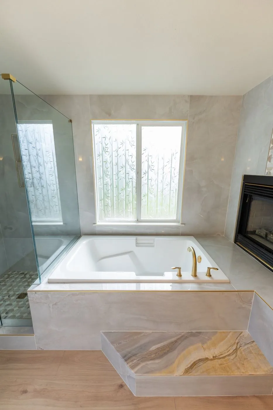 Primary bath with a deep soaking tub beside a gas fireplace and brushed-gold fixtures