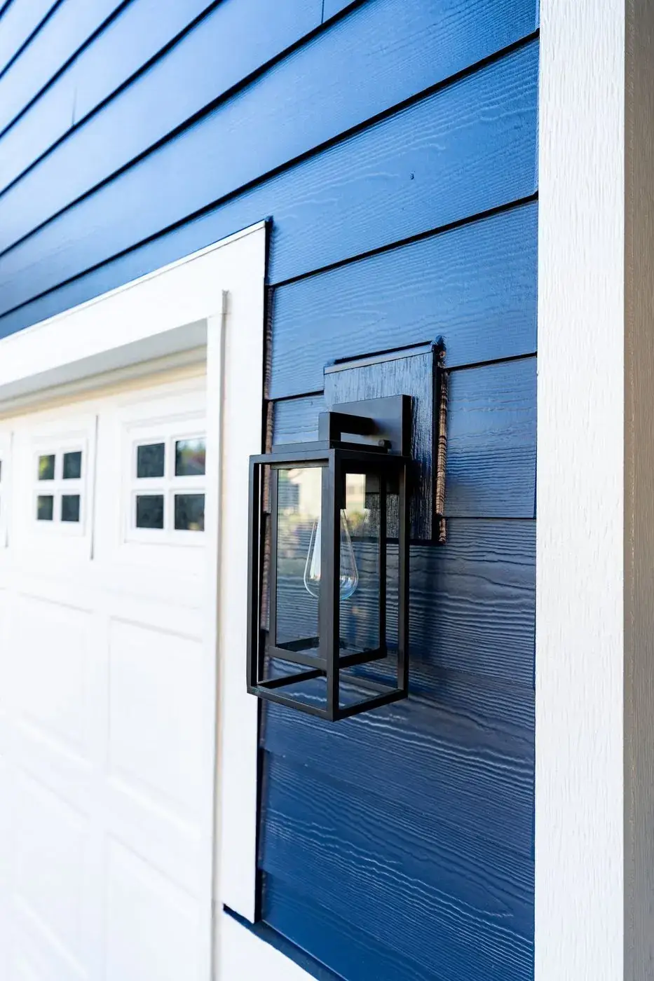 New navy siding with a black wall lantern beside a garage door