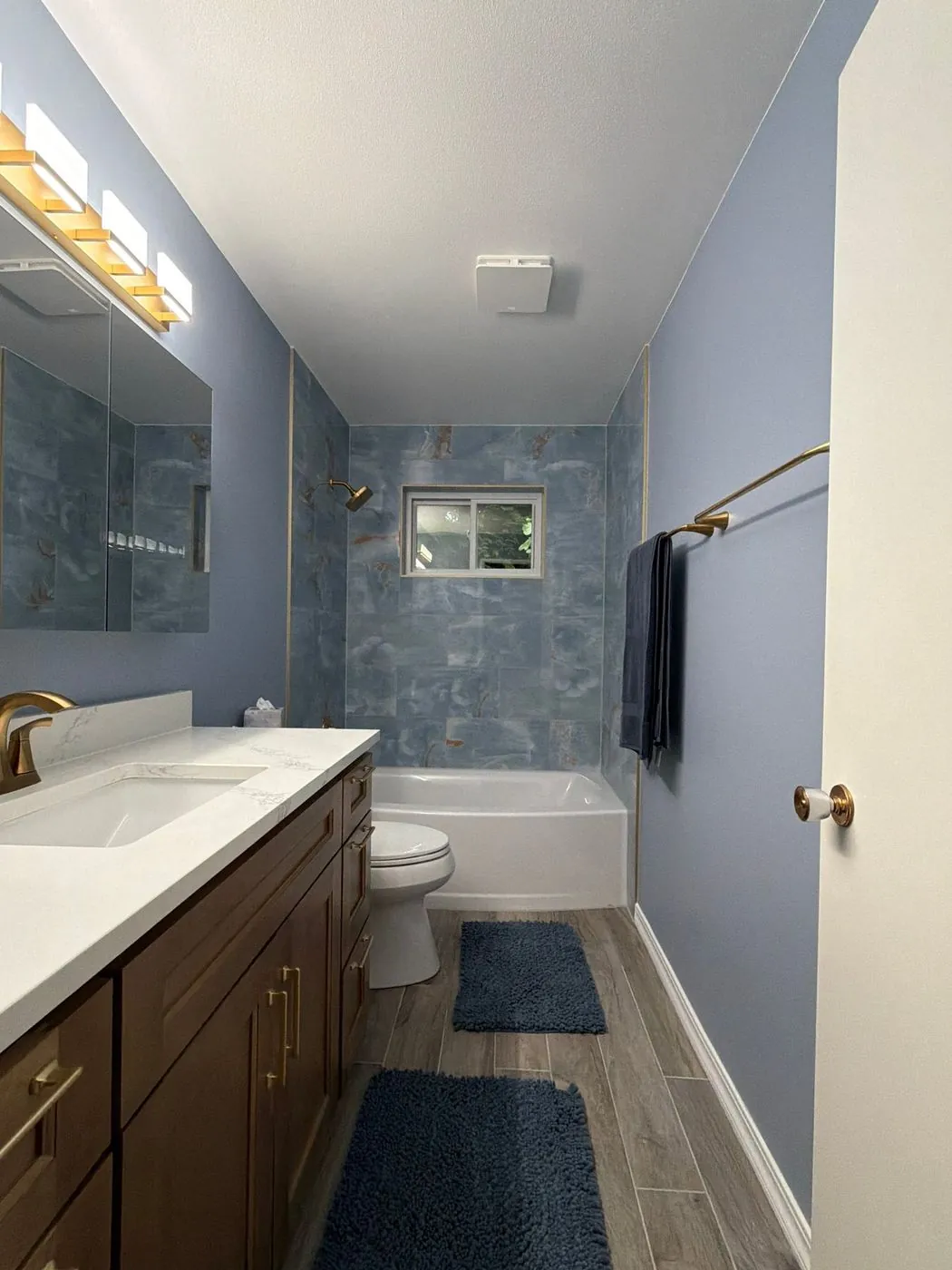 Bath with walnut vanity, marbled blue tub surround and gold fixtures